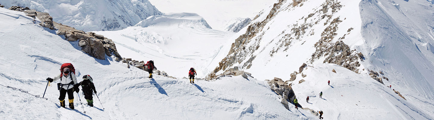 People carrying backpacks hike up a steep, snowy mountain.